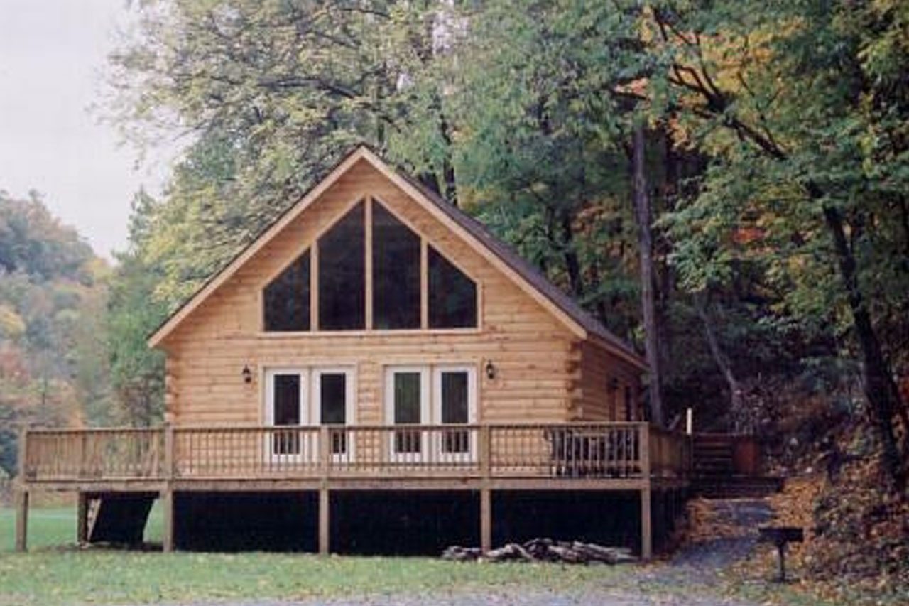 Exterior view of a wooden cabin with large windows and outdoor deck next to a lush forest