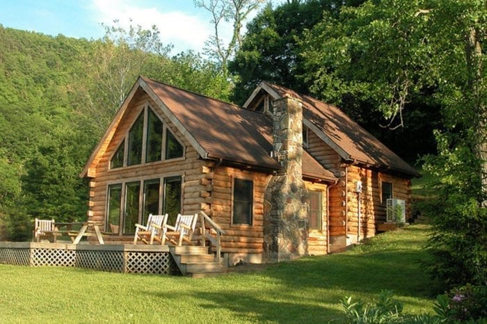 Exterior view of a West Virginia log cabin with large windows, outdoor deck, and stone chimney.