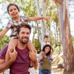 Children Riding On Parent's Shoulders On Countryside Walk.