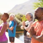 four people meditating with joined hands and closed eyes outside
