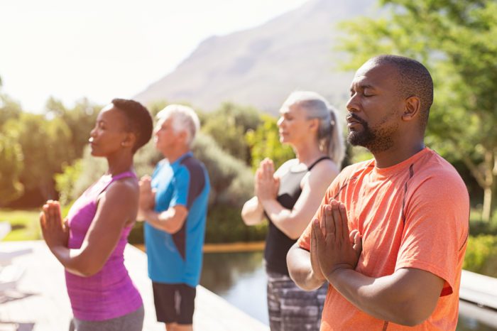 four people meditating with joined hands and closed eyes outside